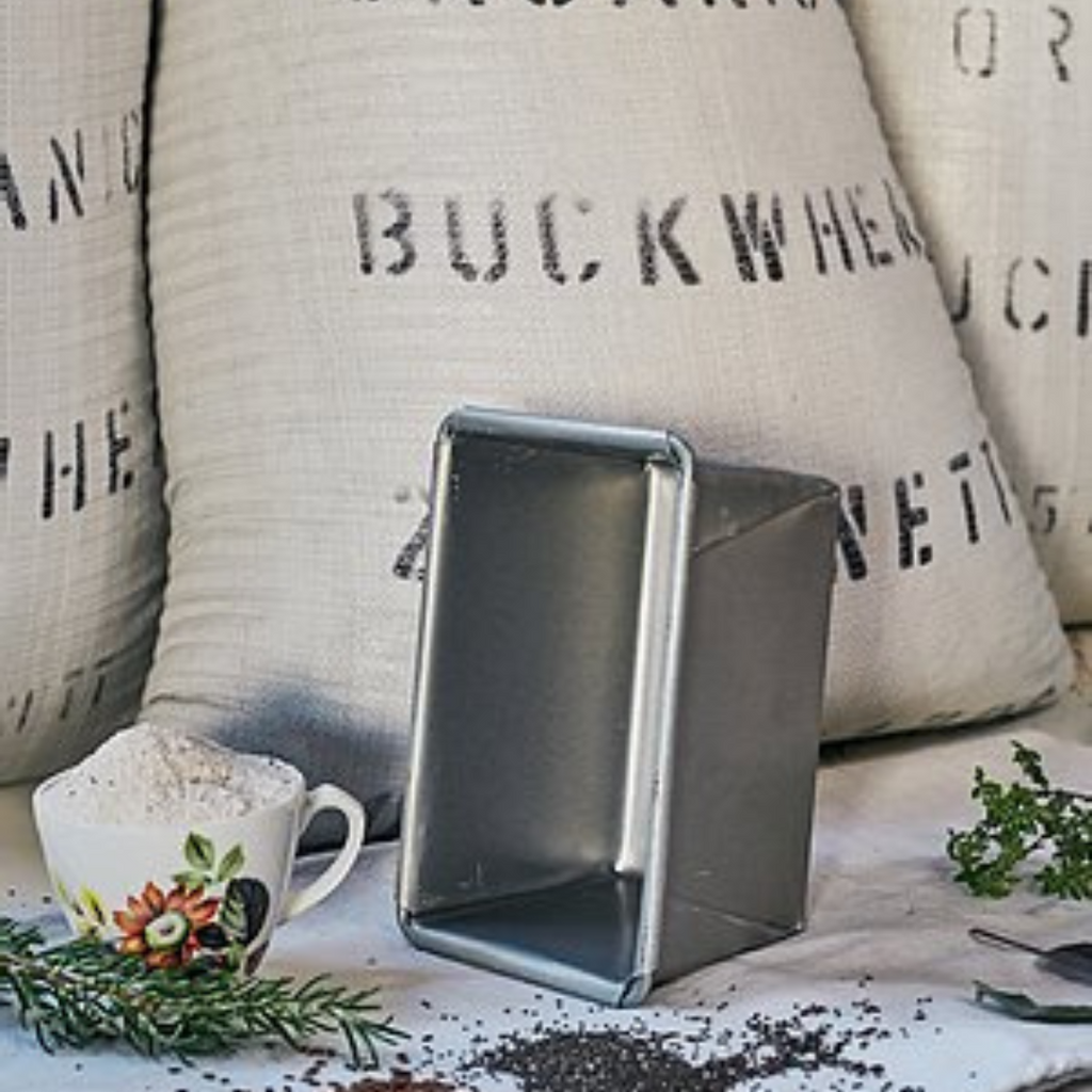 Commercial bread tin, perfect for baking OMGoodness GF/DF Organic bread, standing on it's short edge in front of a sack of organic buckwheat flour with rosemary and dried herbs