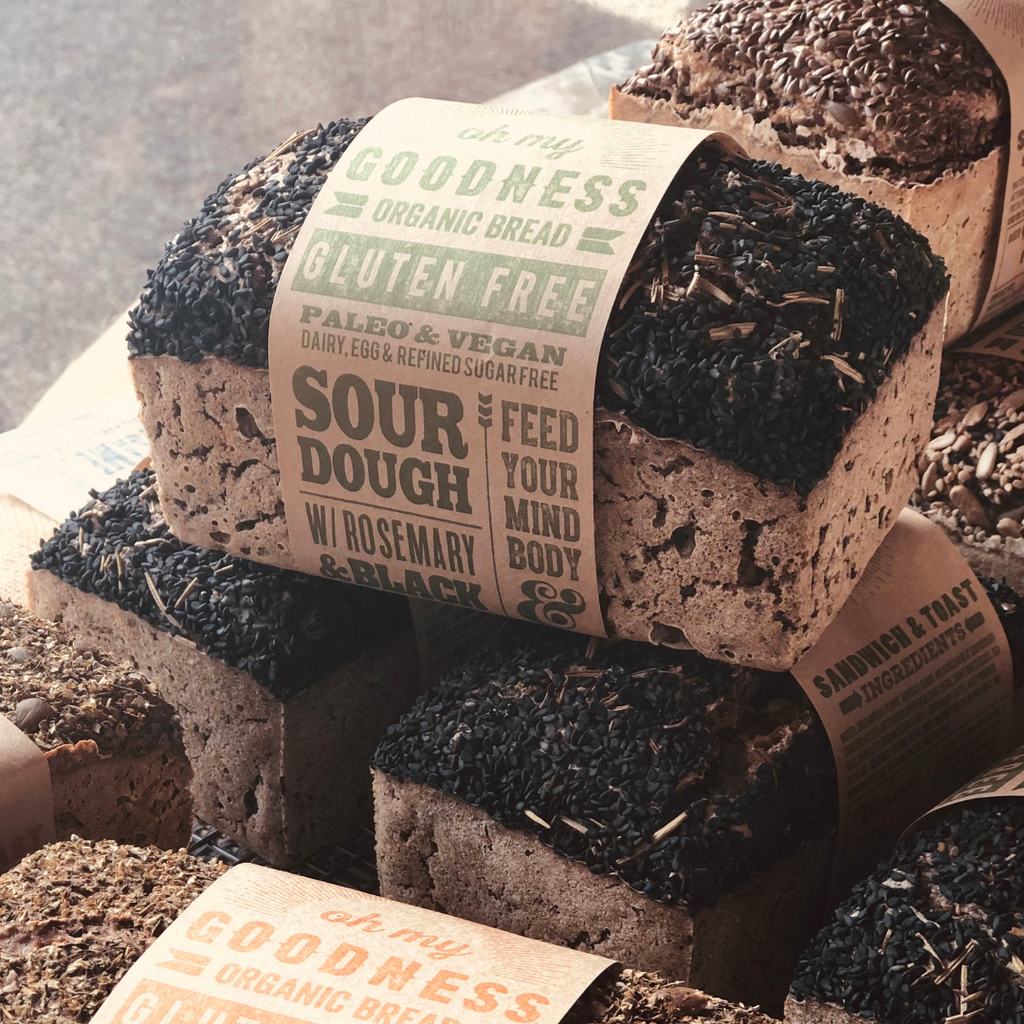 OMGoodness Sourdough w/ Rosemary & Black Sesame GF Organic loaves of bread in a stack.Label reads Gluten Free, Paleo & Vegan, Dairy, Egg & Refined Sugar Free