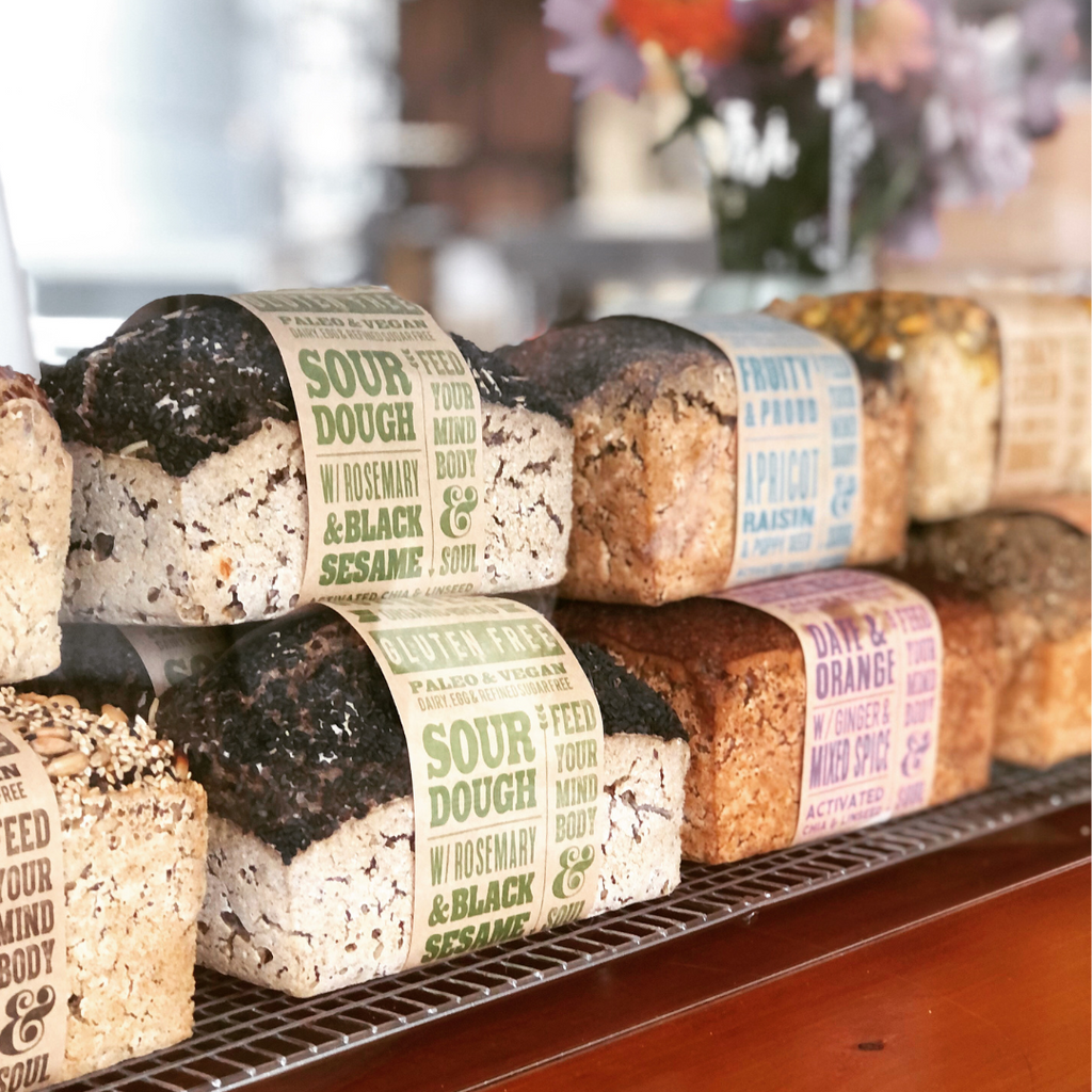 OMGoodness Sourdough w/ Rosemary & Black Sesame GF Organic loaves of bread in a display with other OMG loaves. Label reads Gluten Free, Paleo & Vegan, Dairy, Egg & Refined Sugar Free