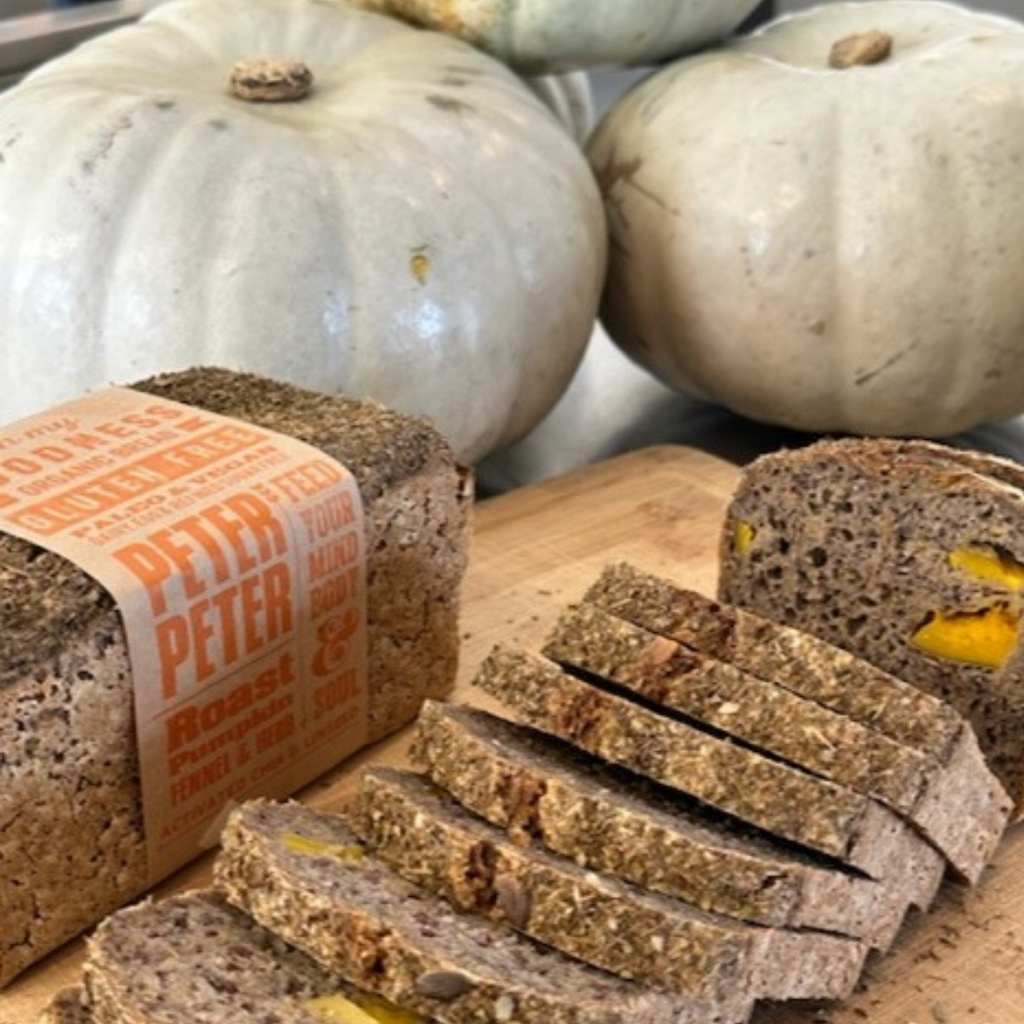 OMGoodness Roast Pumpkin, Fennel & Herb 'Peter, Peter' GF Organic loaf of bread, sliced to reveal roasted pumpkin pieces inside. Fresh whole pumpkins in he background