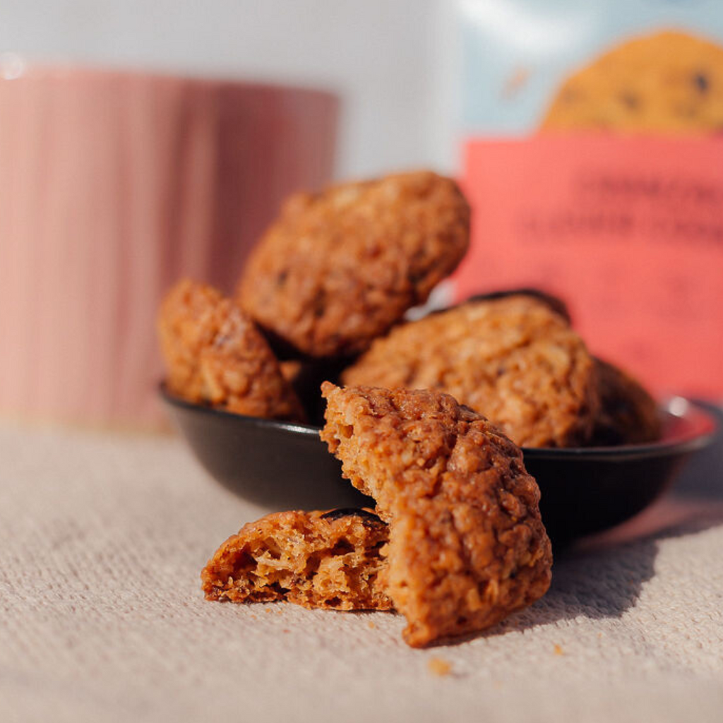 Wisefoods | Cranberry 4.0 Health Star rated & allergen-friendly cookies loose on a pale table mat with an out of focus rose-coloured cup and a Snack Pack in the background