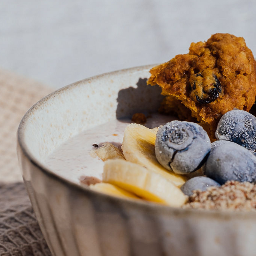 Wisefoods | Close up of a breakfast bowl topped with sliced banana, frozen blueberries and crumbled 4.0 Health Star rated and allergy-friendly, low sugar Fruit & Spice collagen Wise Cookies